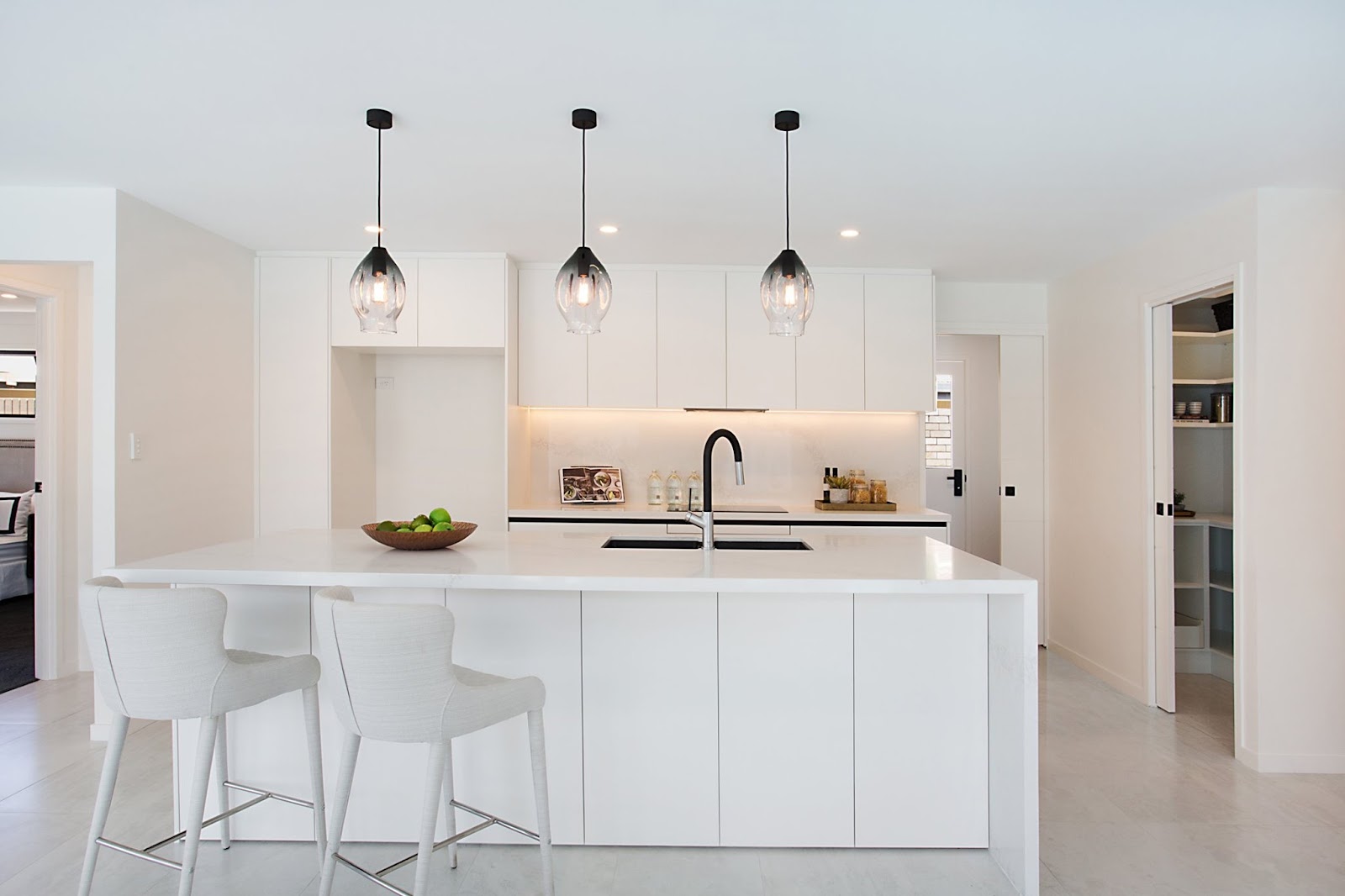 White handleless kitchen with a long island, three glass pendants and black tapware