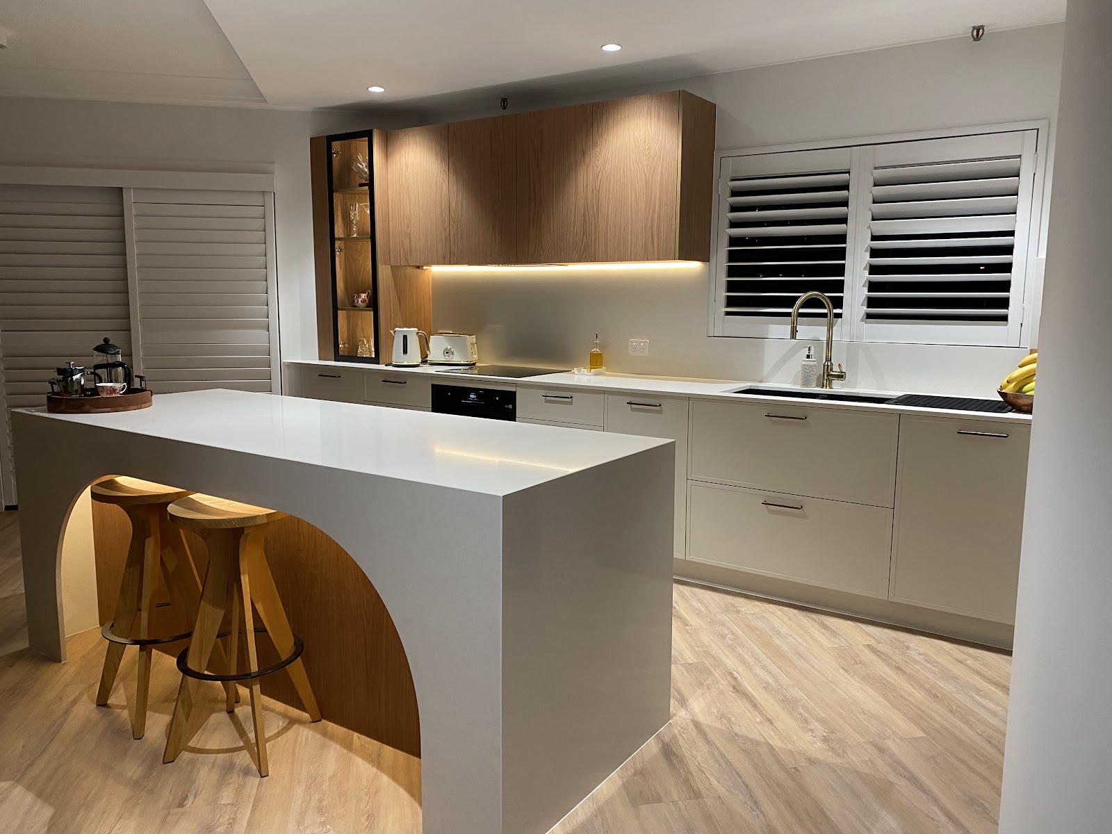 Grey kitchen with a waterfall island, arched timber seat cut-out and timber overhead cabinets