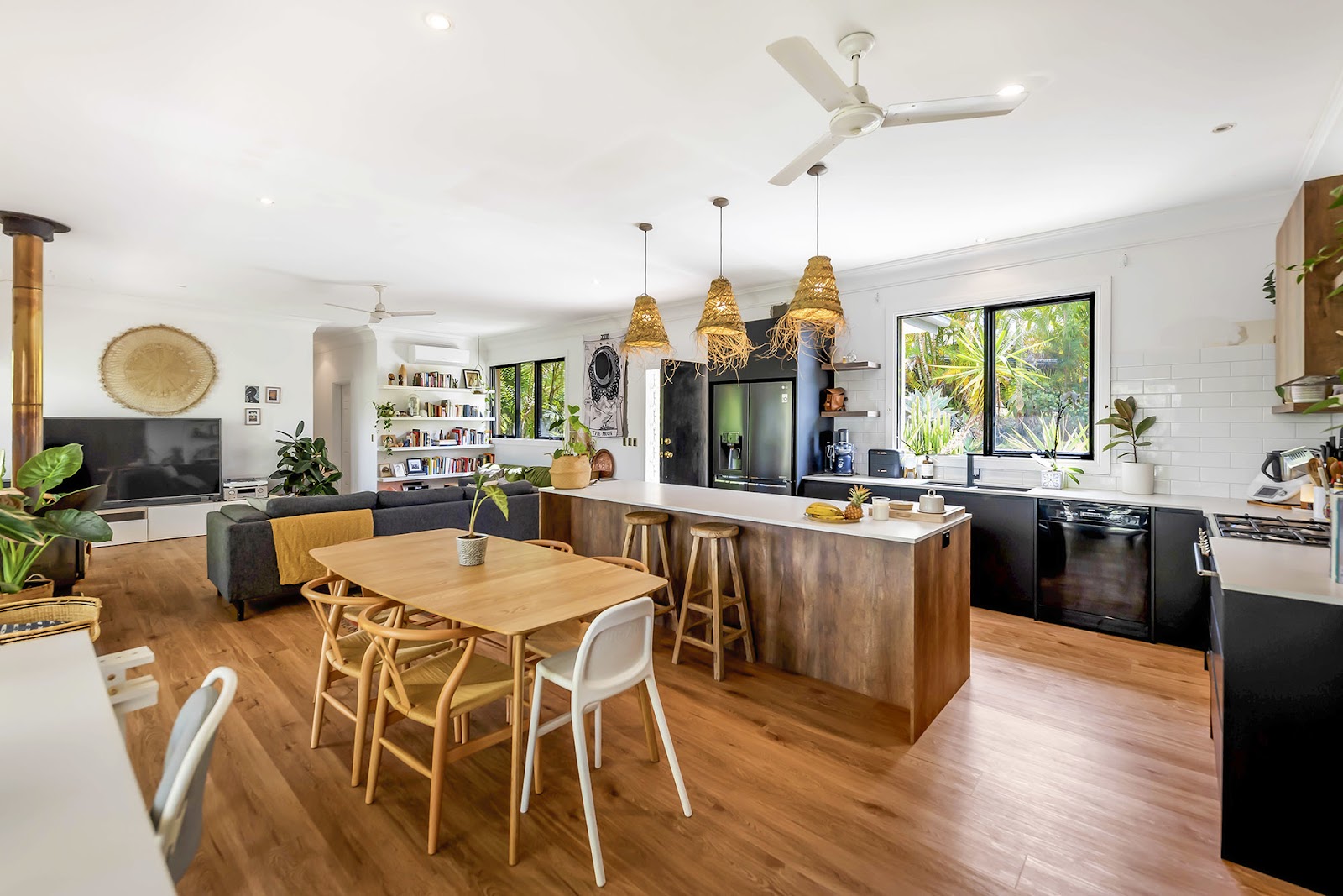 Open-plan living area with a timber and black kitchen island and rattan pendant lights
