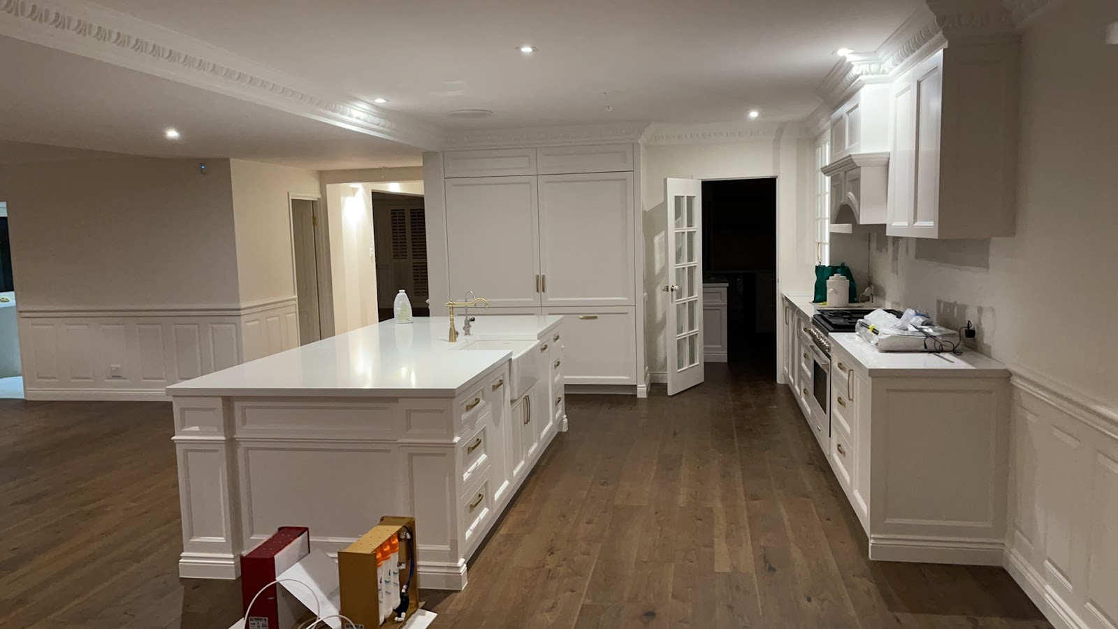 Large white Hamptons-style kitchen with a panelled island on a timber floor