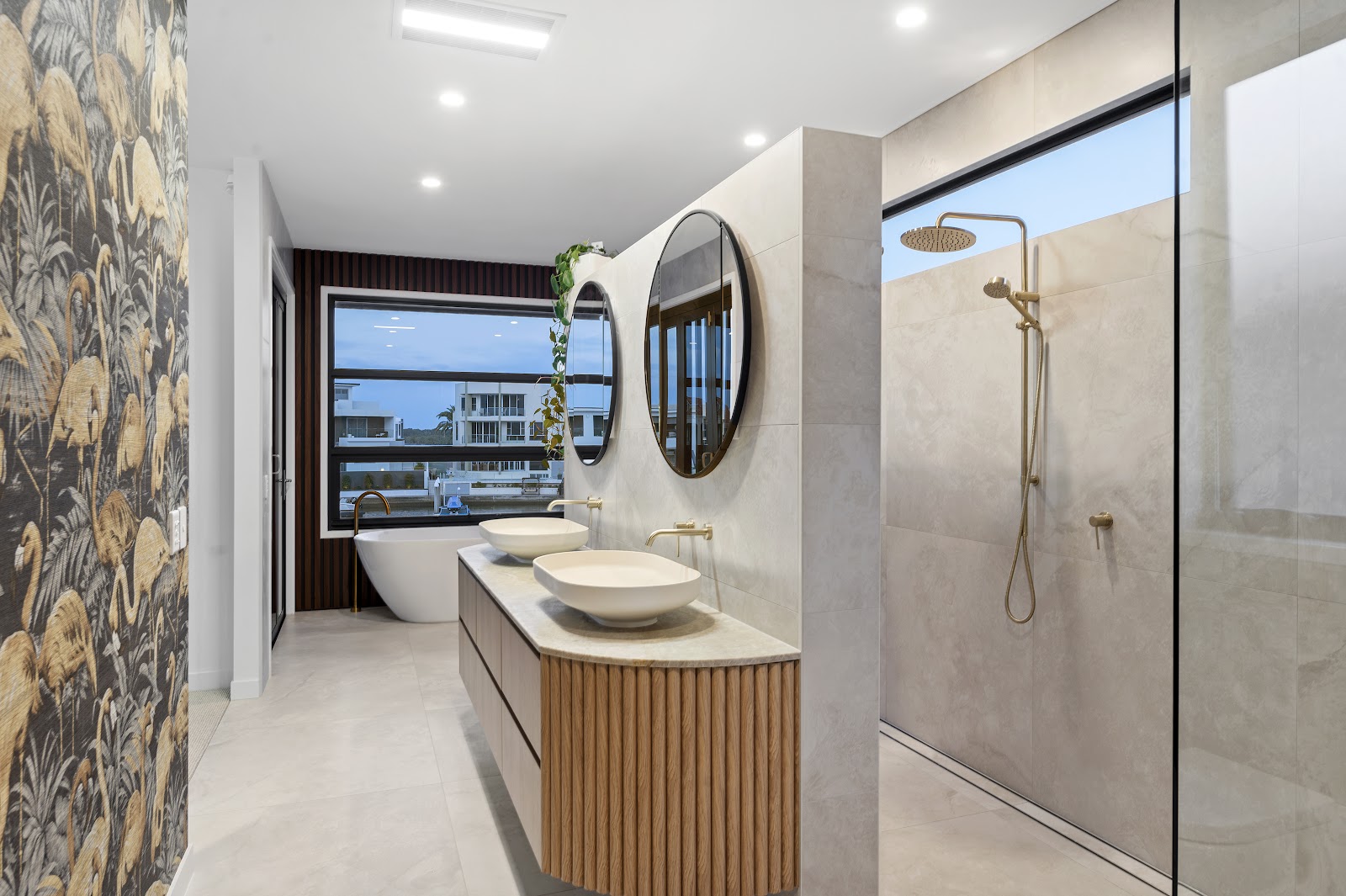 Curved fluted timber vanity with twin basins and round mirrors in a stone bathroom