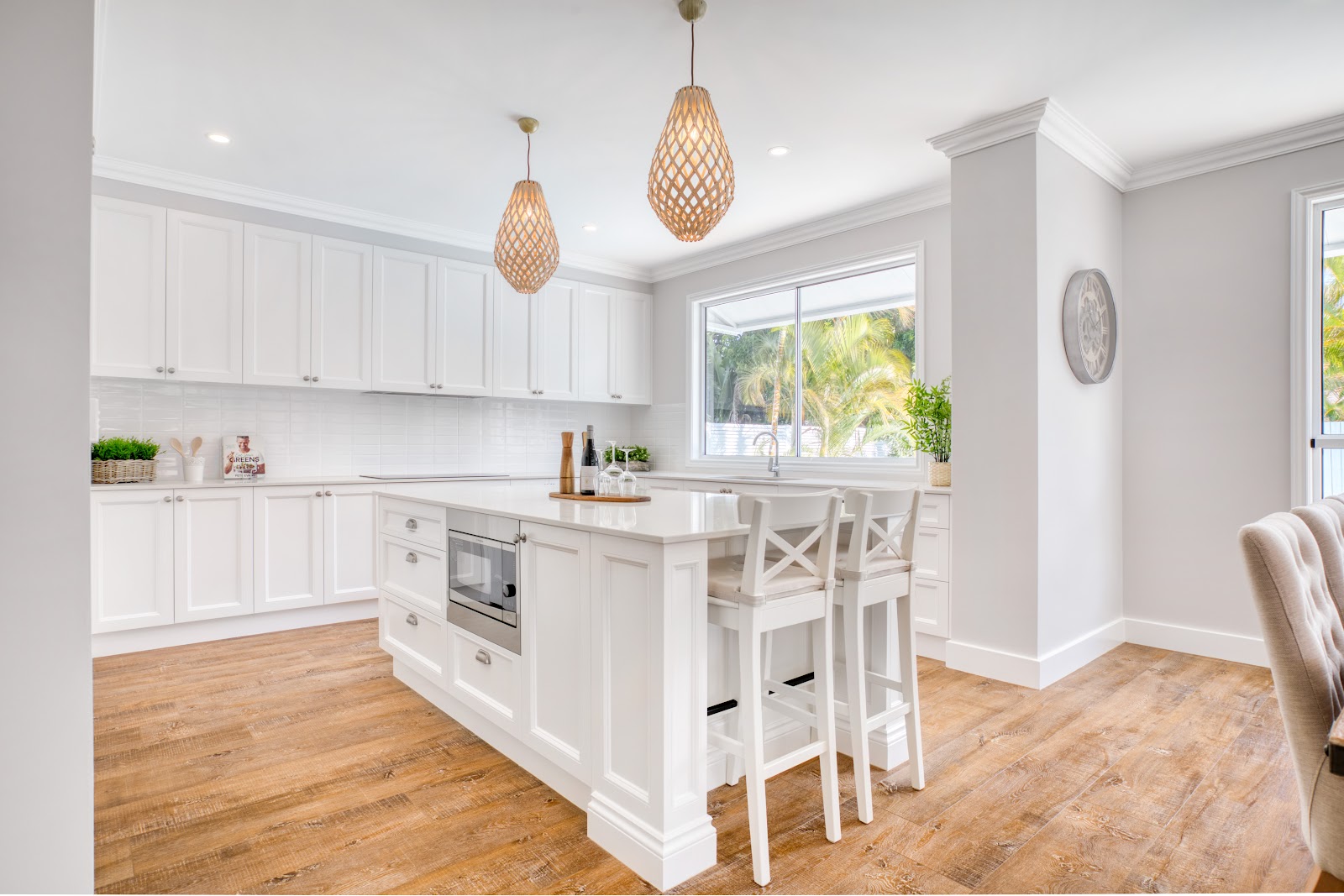 White shaker kitchen with an island bench, bar stools and woven pendant lights